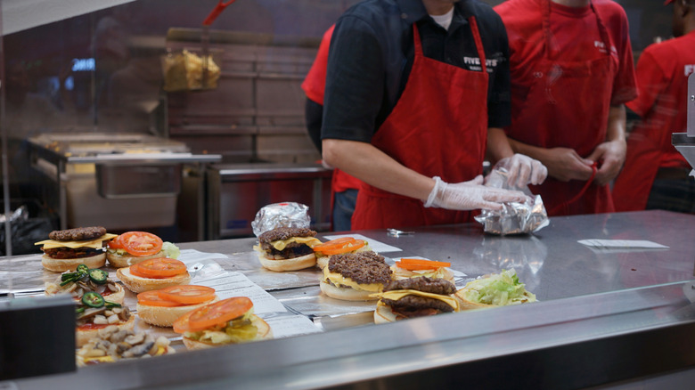 Five Guys employee prepping burgers in restaurant kitchen.