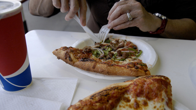 Customer eating Costco pizza in food court with plastic fork and knife.