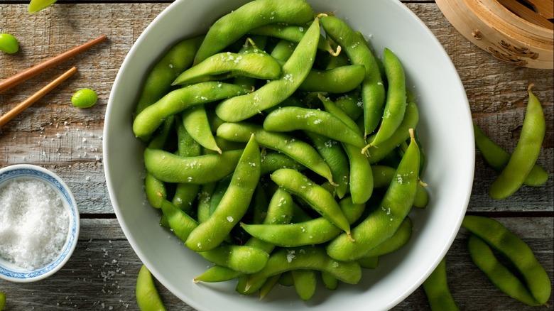 Edamame in white bowl next to chopsticks