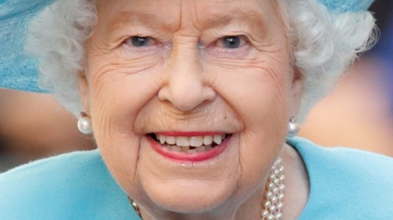 Queen Elizabeth II smiling while wearing blue hat and pearl earrings