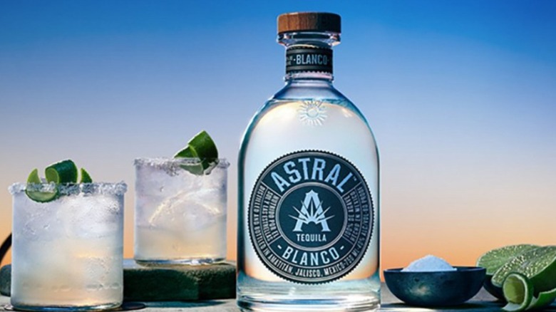 Astral Tequila bottle with cocktail glasses, salt, and lime