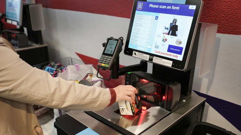 A closeup of an Aldi self-checkout register with a computer screen and person scanning item