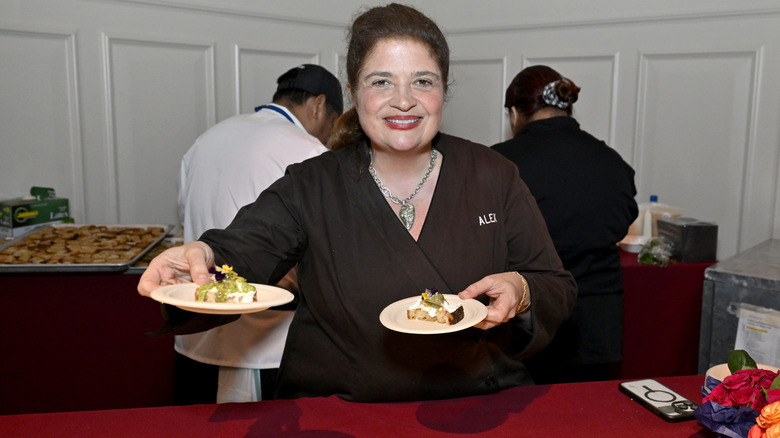 Alex Guarnaschelli holding up two dishes at food event.