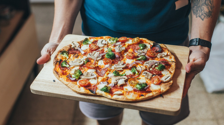 A person holding a wooden tray with a veggie pizza flatbread on top