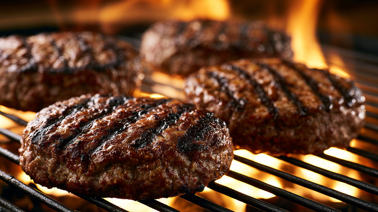 Four seared burger patties on flaming grill.