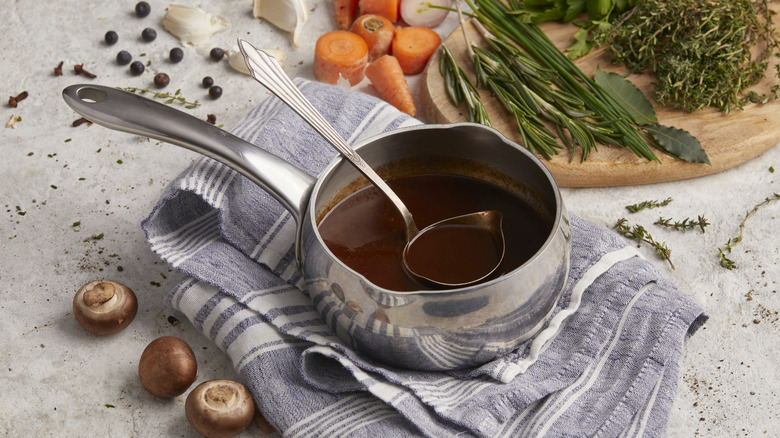 Saucepan of au jus with ladle surrounded by ingredients.