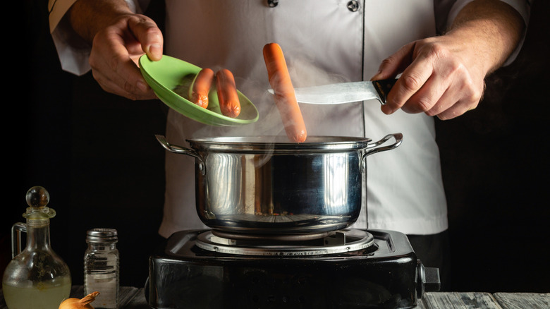 Chef steaming hot dogs in pot with one dog on knife
