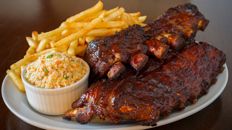 A rack of barbecue ribs with fries and coleslaw
