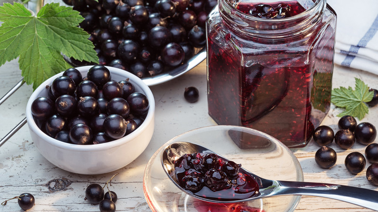 Fresh black currents in bowls along with a jar of black currant jam with spoon