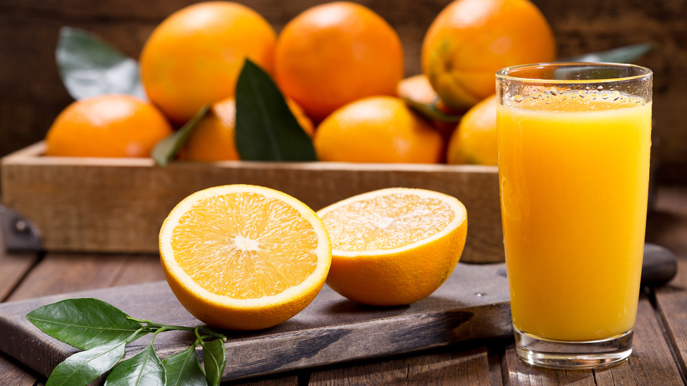 Oranges, whole and halved, next to glass of orange juice