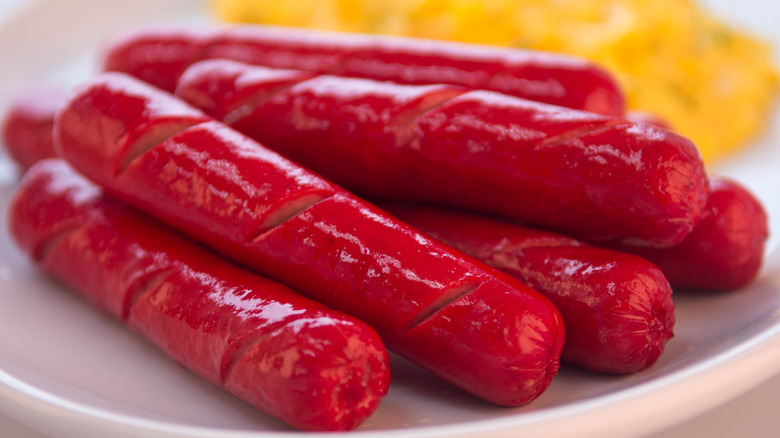 A pile of red hot dogs on a white plate.