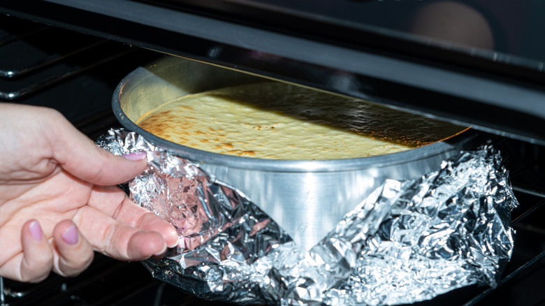Hands removing cheesecake from oven