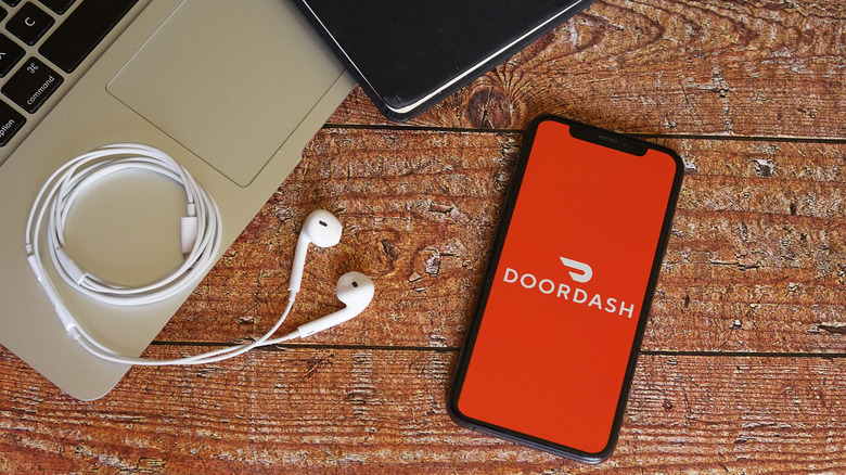 DoorDash app on phone next to laptop and headphones