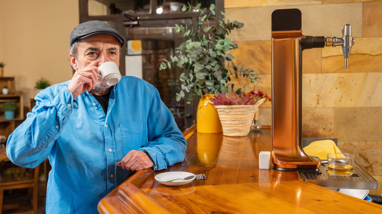 Customer standing, drinking coffee at bar