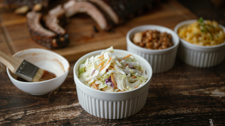 Ramekin of coleslaw featured in front of BBQ ribs with other sides of baked beans and mac & cheese