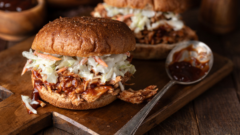 Pulled chicken BBQ sandwich with coleslaw on top of the chicken and a spoon of BBQ sauce on the side