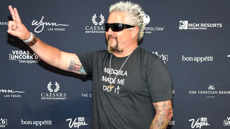 Guy Fieri holding a peace sign wearing sunglasses