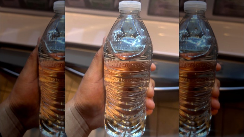 A hand holds a water bottle that has the Kirkland label embedded into the plastic itself.