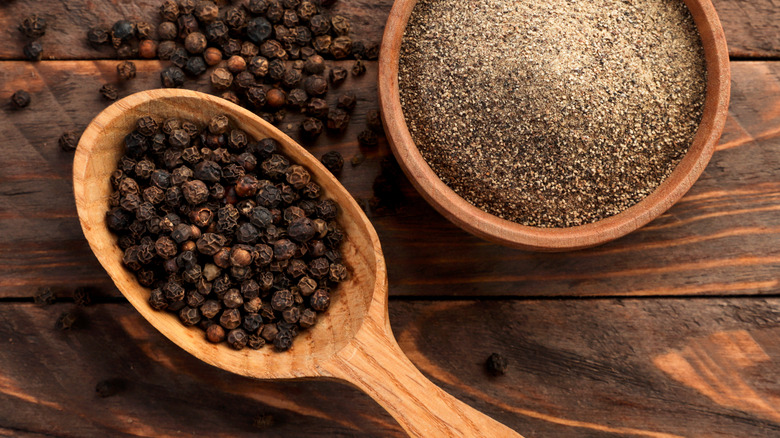 Black peppercorns next to a bowl of cracked pepper