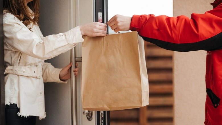 delivery person handing bag of food to woman