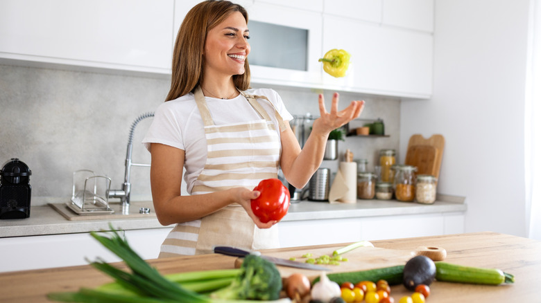 Woman holding and tossing peppers in kitchen