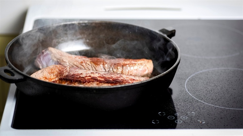 Steaks being seared on a cast iron skillet over an induction cooktop.