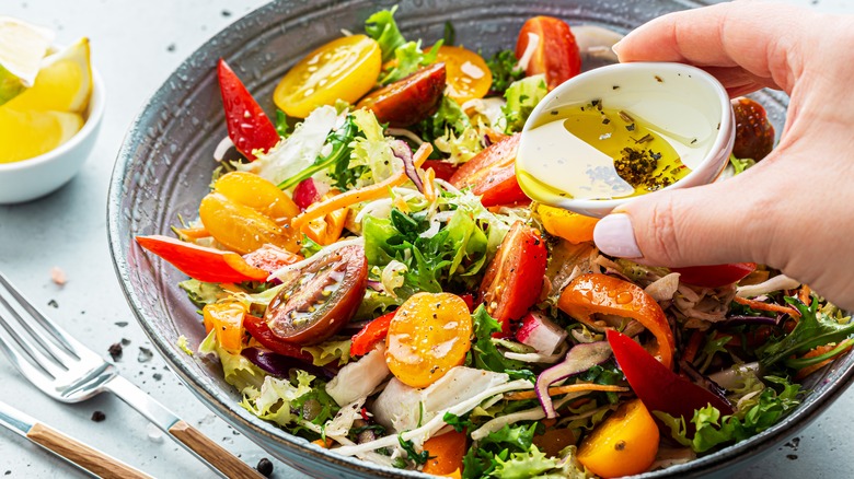 hand adding dressing to salad