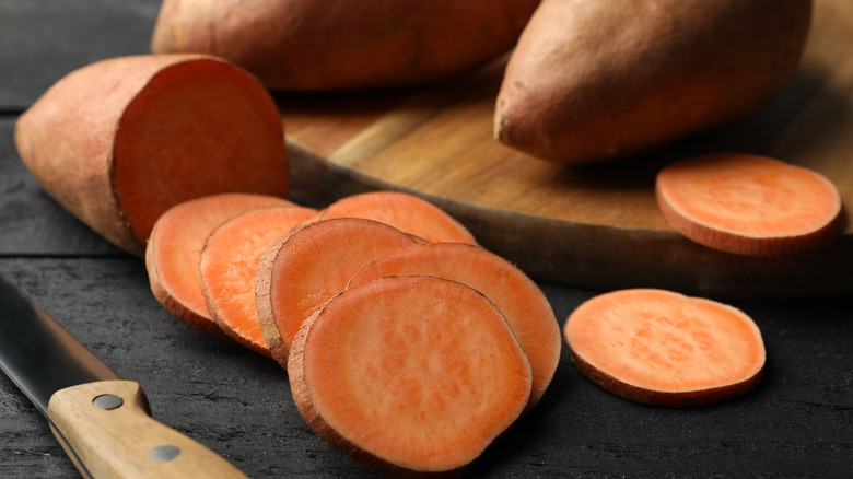 A sliced sweet potato at the forefront with two whole ones in the background