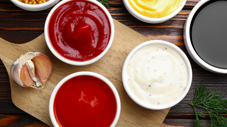 A variety of dips including ranch and ketchup on a wooden table with cutting board
