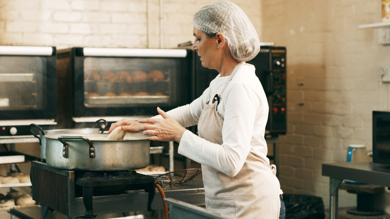 Woman in hairnet frying donuts in bakery