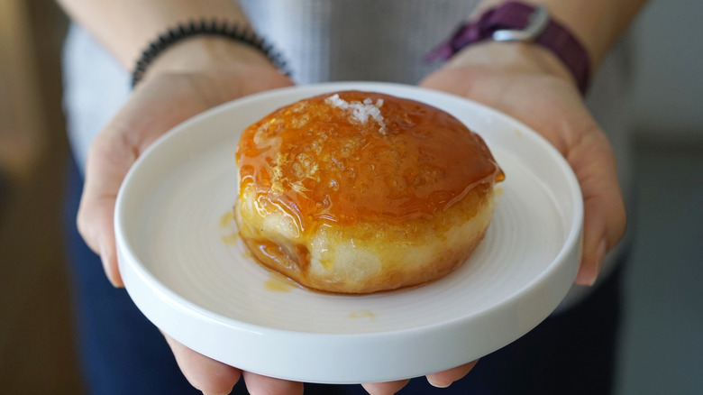 Hands holding a caramel donut on a plate with sea salt sprinkled on top