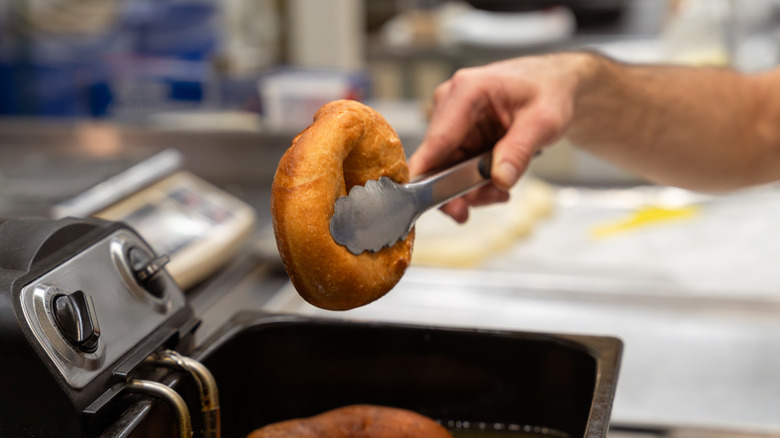 Hand removing donut from fryer with tongs