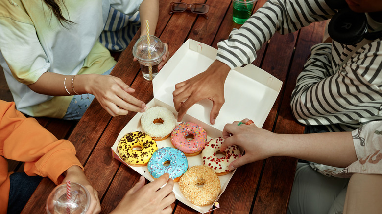 Hands reaching for donuts from a box
