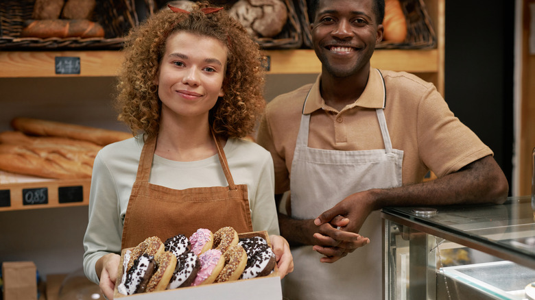 Two bakers posing for camera, one holding a box of donuts