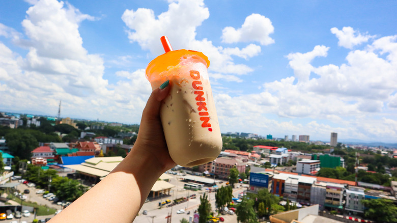 A hand holding a Dunkin' iced coffee in the air