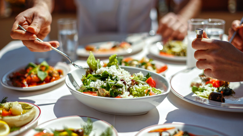 Person taking a fork of salad with other food dishes surrounding the plate