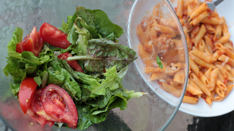 Salad with lettuce and tomatoes with a pasta dish behind it