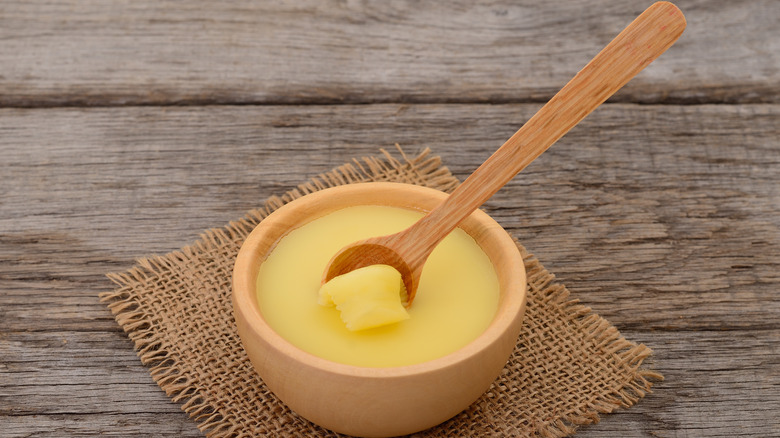 Ghee in a wooden bowl with a wooden spoon scooping some out