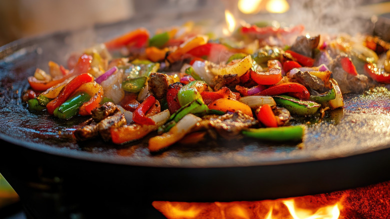 Fajitas being cooked on a flat top griddle over a flame