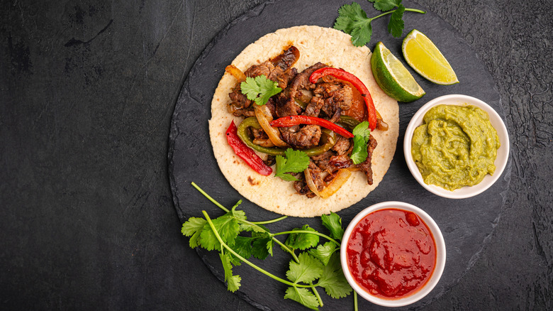 Beef fajitas garnished with cilantro and lime wedges next to bowls of salsa and guacamole
