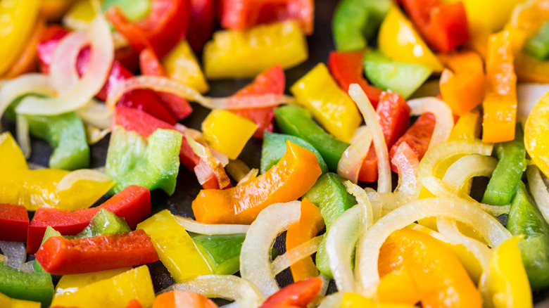 Sliced bell peppers of all colors and onions cooking in a pan