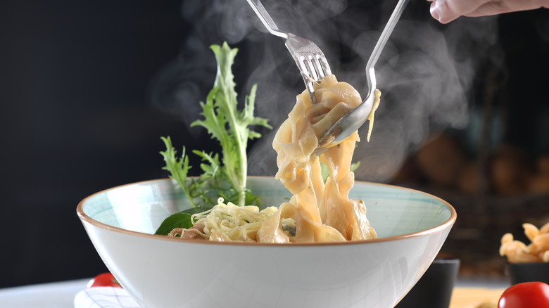 hands twirling fettucine Alfredo onto a fork