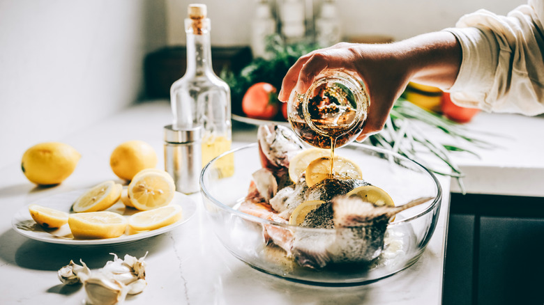 woman marinating whole fish with lemon and oil in a glass dish