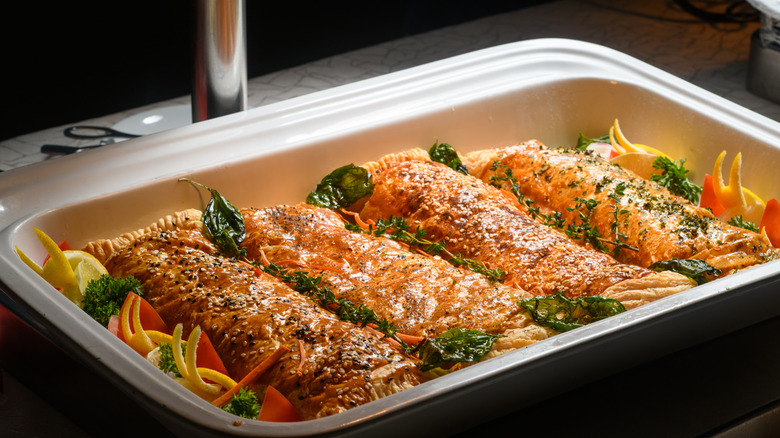 salmon fillets in a baking dish surrounded by vegetables, herbs, and lemon