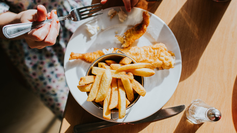 Person eating a plate of fish and chips at a restaurant