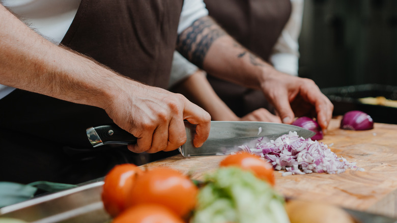 professional chef chopping red onions on a wooden cutting board