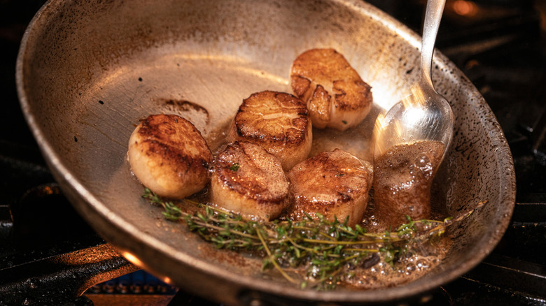 scallops being pan-seared in a pan with butter and herbs