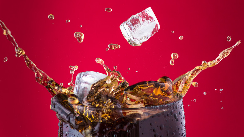 Glass of Coca-Cola with ice being dropped in