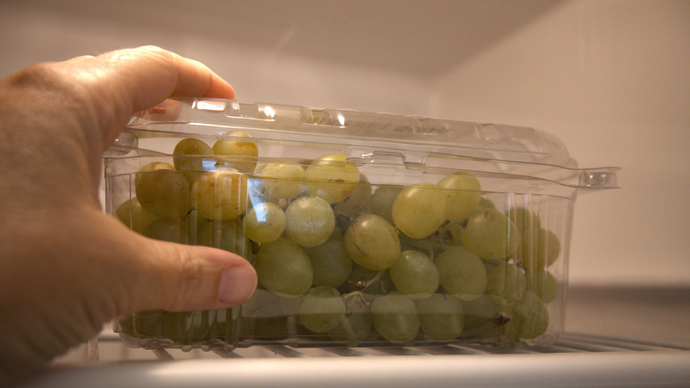 Hand grabbing green grapes in plastic container in fridge