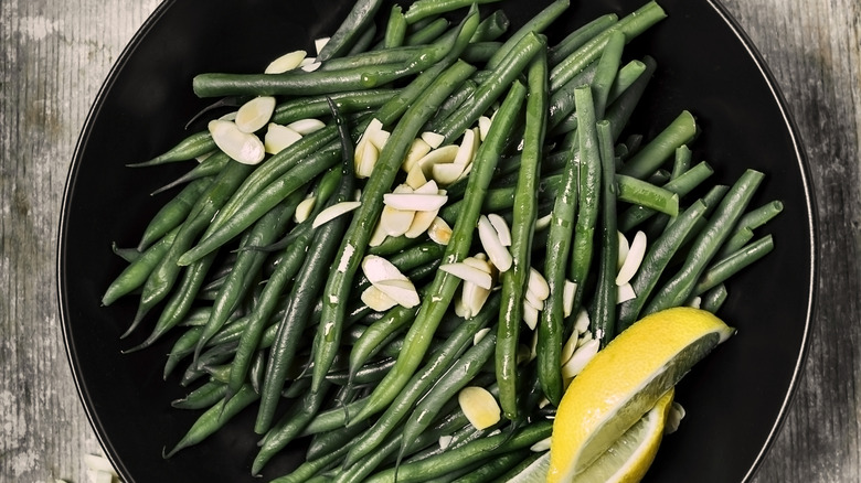 Nuts are sliced over green beans that fill a black bowl.